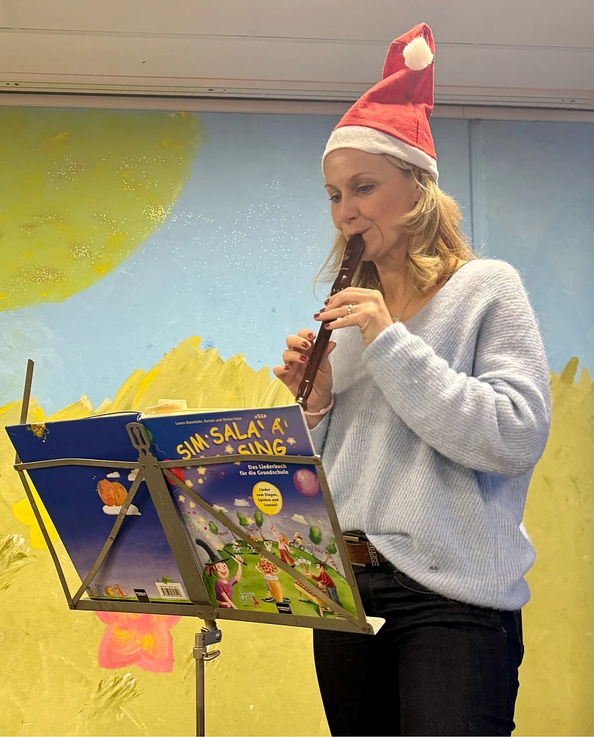 Eine Lehrerin begleitet die Kinder musikalisch mit einer Flöte. 