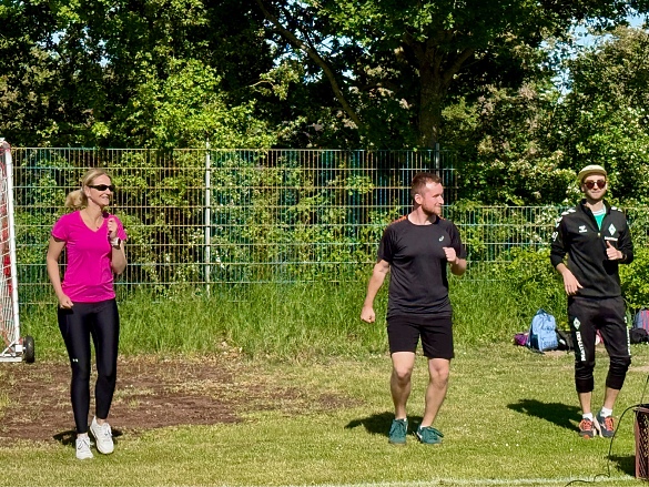 Drei Lehrkräfte leiten die Aufwärmübung an. 
