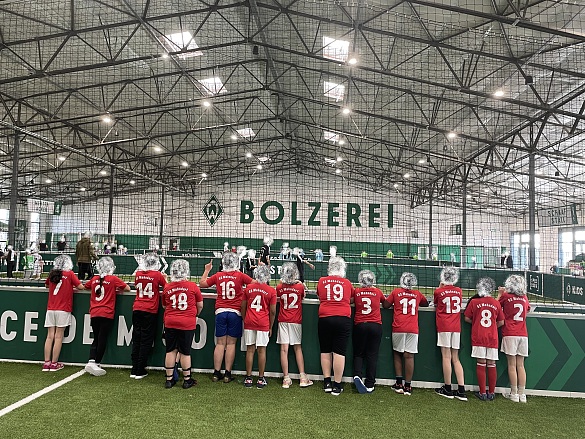 Ein Foto von der Mannschaft von hinten. Die Kinder tragen rote Trikots der Schule von der Sparkasse. Die Gesichter sind unkenntlich. 