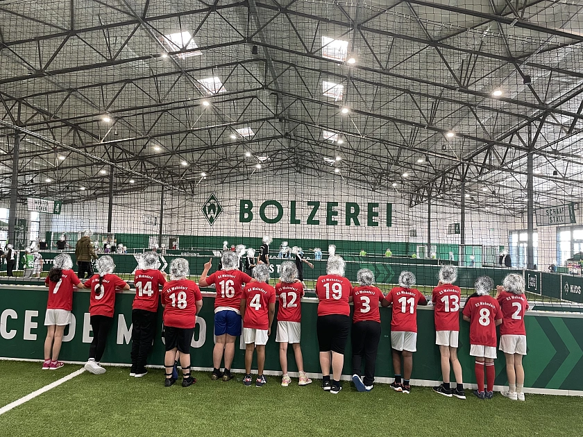 Ein Foto von der Mannschaft von hinten. Die Kinder tragen rote Trikots der Schule von der Sparkasse. Die Gesichter sind unkenntlich. 